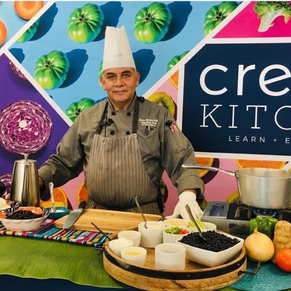Chef standing behind a table with various fresh ingredients and kitchen utensils on it.